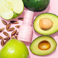 A bottle of Saturday Skin Wide Awake Brightening Eye Cream surrounded by key ingredients of the formula, such as green apples, avocado, and date seeds