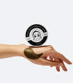 Someone balances a container of Shangpree Gold Black Pearl Eye Mask on the back of their hand, with one of the eye masks applied to their hand, showing how the product sticks and molds to the skin