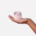 Someone holds a jar of Peach & Lily Pore Proof Perfecting Clay Mask and smears some of the mask on their wrist to show the thick, clay texture and easy application